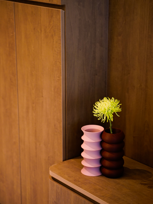 Two nestled vases, one in color rosé and the other in russet, with sleek glass inserts, displayed on a wooden surface.